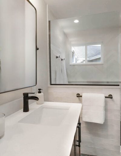 Modern bathroom interior with white and gray tiles, featuring a sink, mirror, and glass shower enclosure, decorated with a green potted plant.