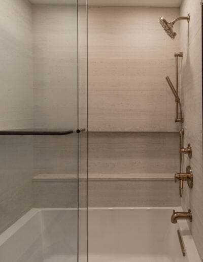 Glass-enclosed tub shower with brushed gold hand shower and rainfall head