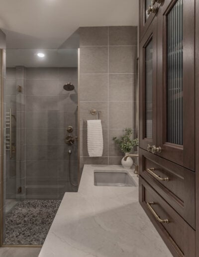 View through the primary bathroom to a curbless tile shower and custom cabinetry