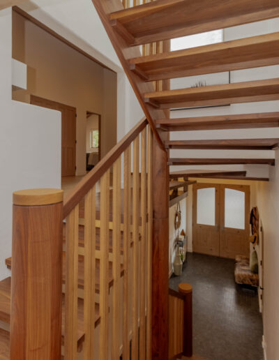 Open-riser walnut staircase with a curved slatted wood guardrail, seen from the landing toward the entry doors
