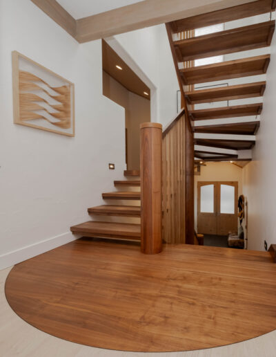Entry hall with floating walnut stair treads, a round walnut newel post and a curved walnut inlay in the pale oak floor