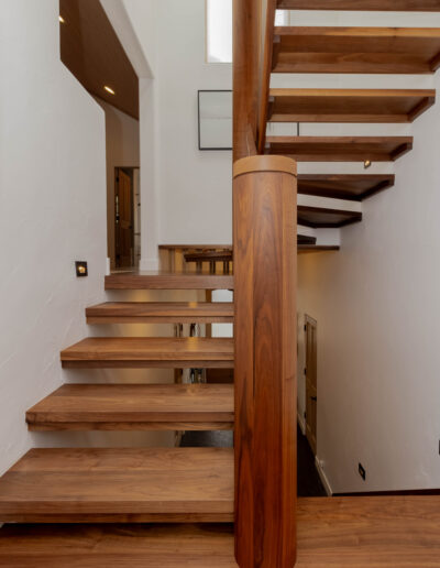 Floating walnut stair treads wrapping a round walnut column between two levels