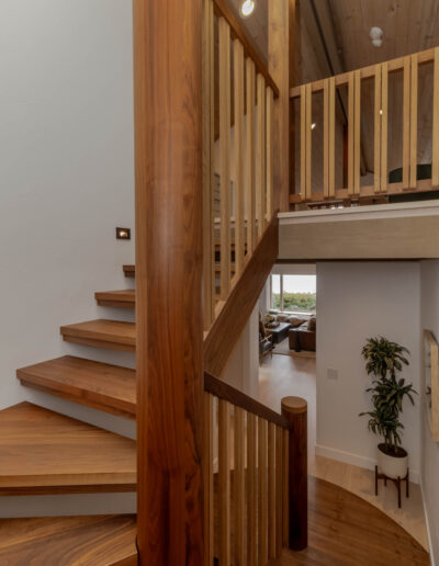 Curved walnut stair rail with vertical wood balusters, open to the loft and the living room below