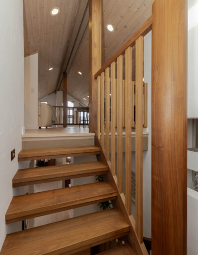 Walnut open-riser stairs climbing to a loft under a wood plank ceiling