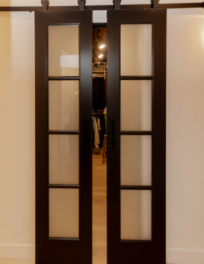 Black-framed sliding doors with frosted glass panels on barn-door hardware, opening to a walk-in closet