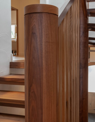 Round walnut newel post and vertical wood balusters at the foot of the stairs