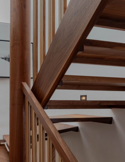 Detail of walnut stair treads and stringers seen through the slatted guardrail