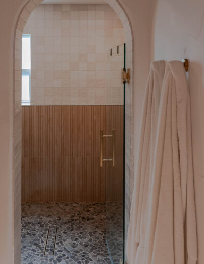 Arched shower entry with a frameless glass door, brass handle and pebble stone floor