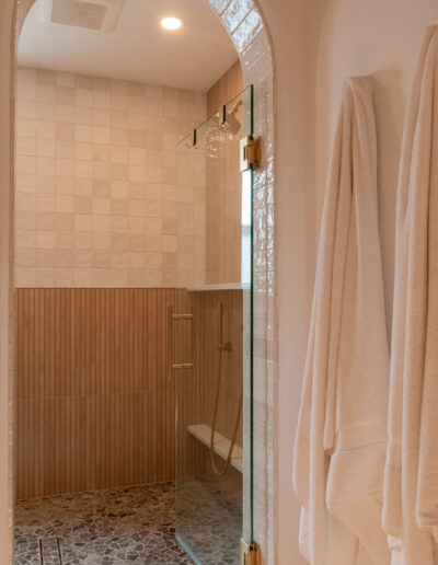 Arched walk-in shower with brass hardware, a pebble floor, a bench and white towels on hooks